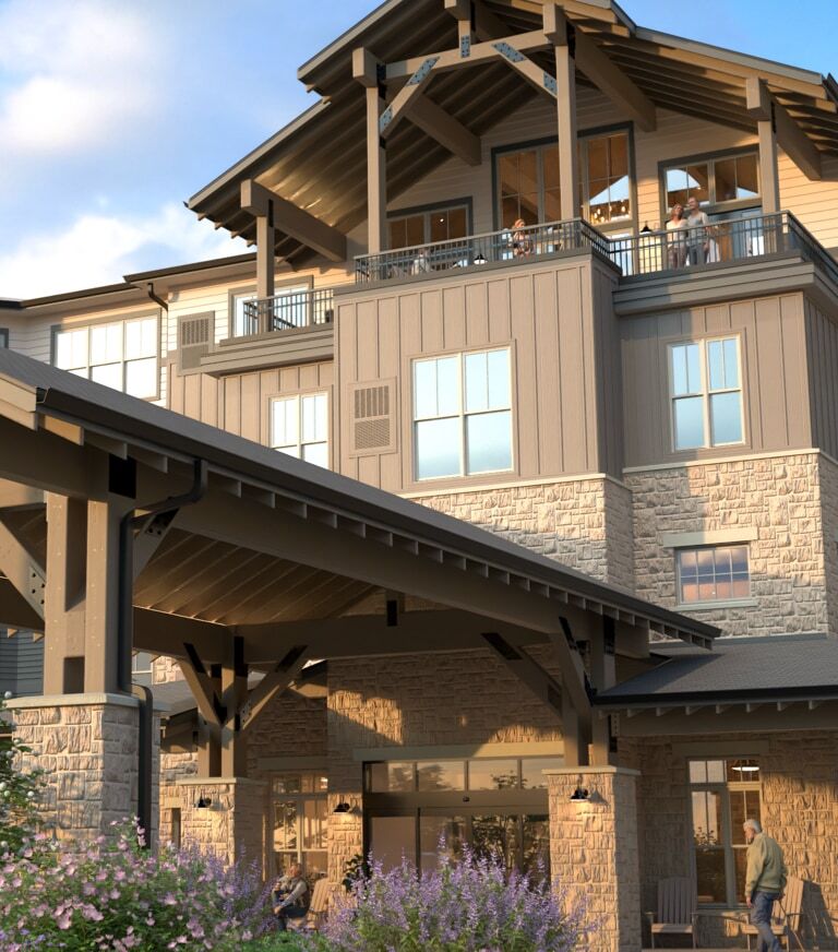 A lodge-style building with a large covered entrance and landscaped flower beds in the foreground.